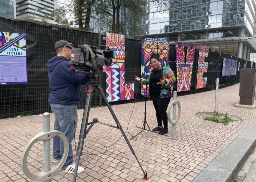 A camera man interviewing an artist on the street next to the Love Letters public art  exhibition