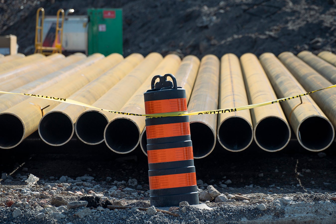 Pipes in a construction site behind a traffic cone. 