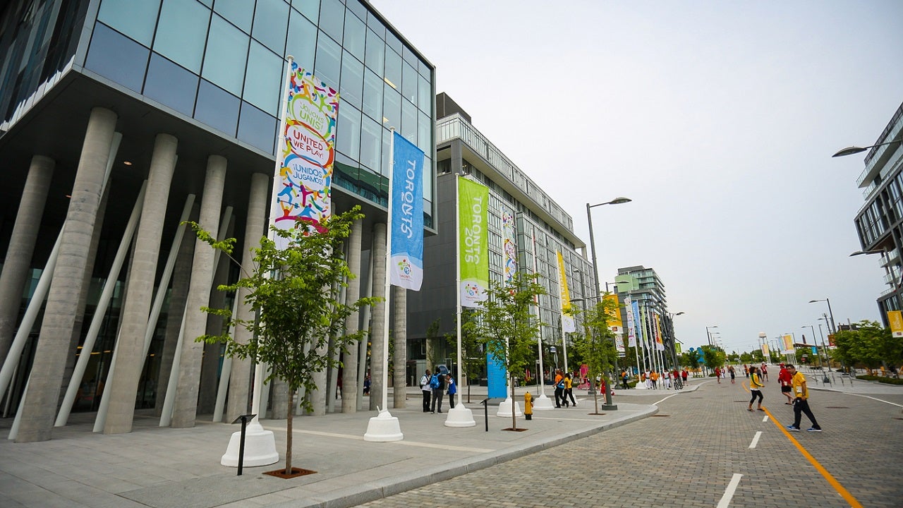 Photograph of street with people walking around and entering buildings on the left side.