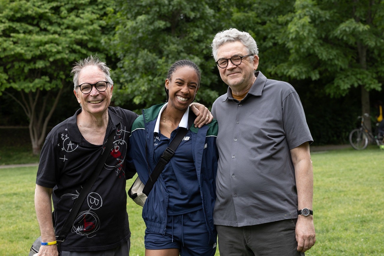 Three individuals posing together at the camera in a park.