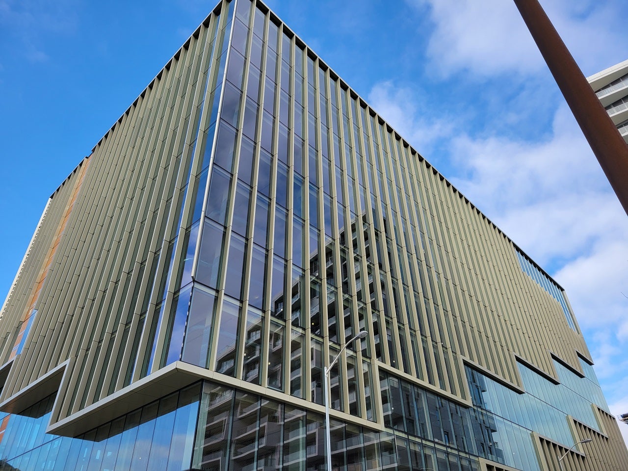 Modern glass building with vertical louvers made of mass timber under a clear blue sky.