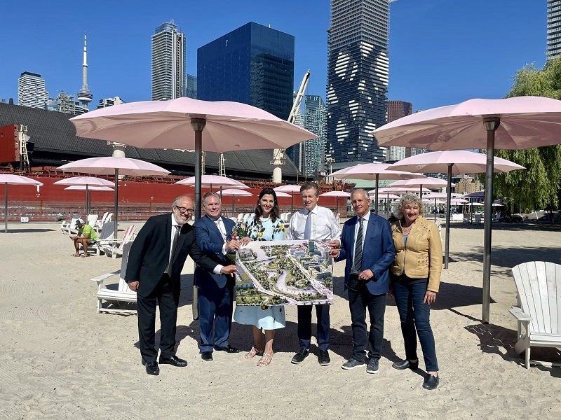 Six individuals posing while holding a poster of Lassonde Art Trail with pink umbrellas and buildings in the backdrop.