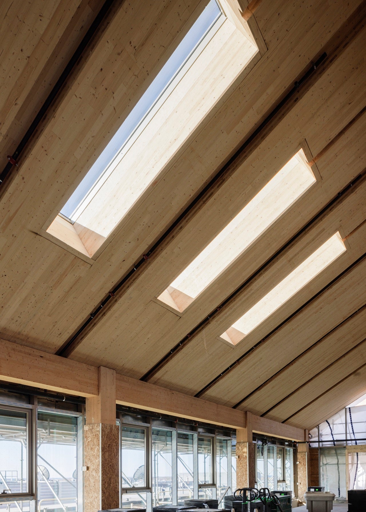 Interior of a modern building featuring sloped mass timber ceilings with skylights and large windows, bathing the space in natural light.