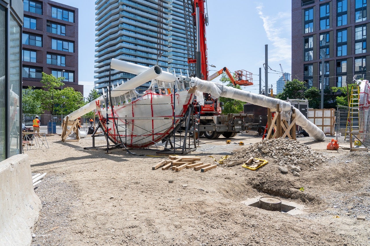 An art piece with long cylindrical legs is placed in the middle of a construction site.