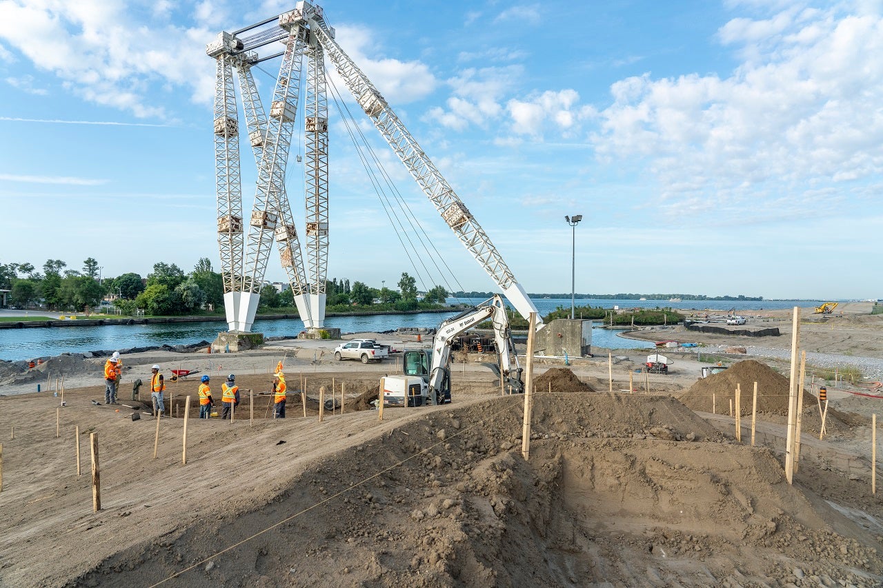 A tall crane in the middle of a construction site surrounded by crew members. 