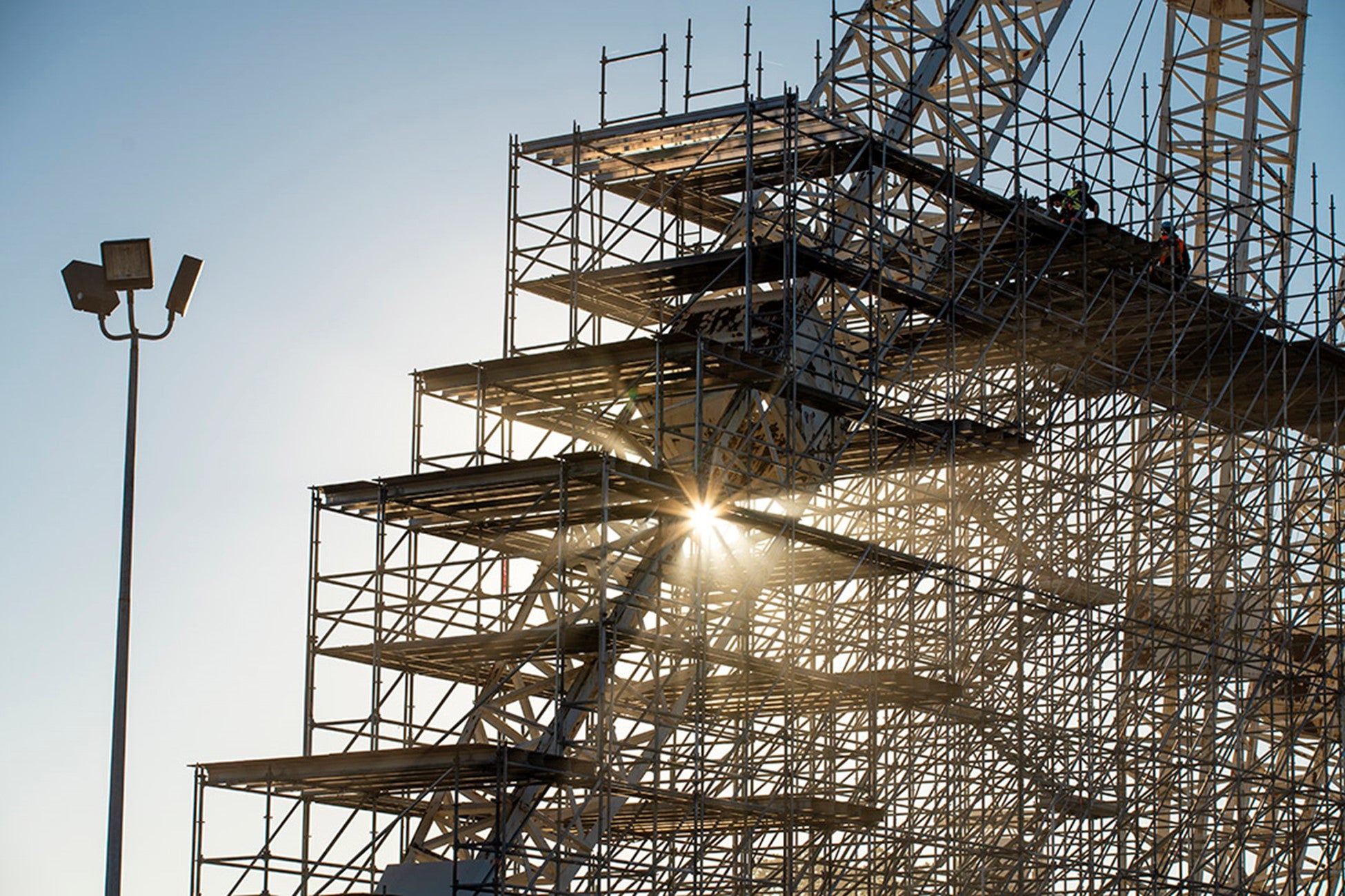  Sunlight piercing through a step wise metal structure of a crane with scaffolding. A lamp post on the left. 