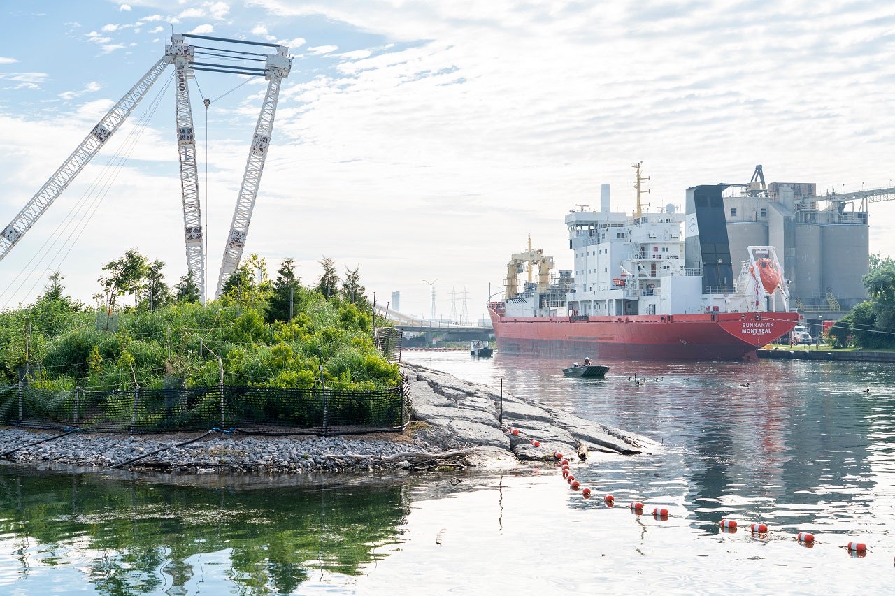 Island on river's edge with a massive crane in the left, a ship and cement cubicles on the left.