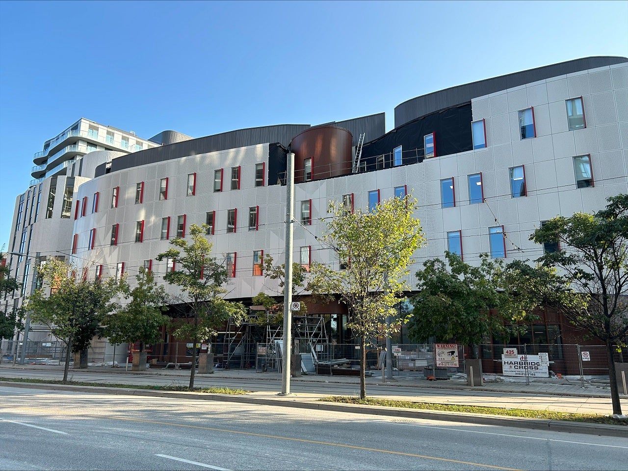 A building across the side of a street. There is a pole in between and trees run along the street.