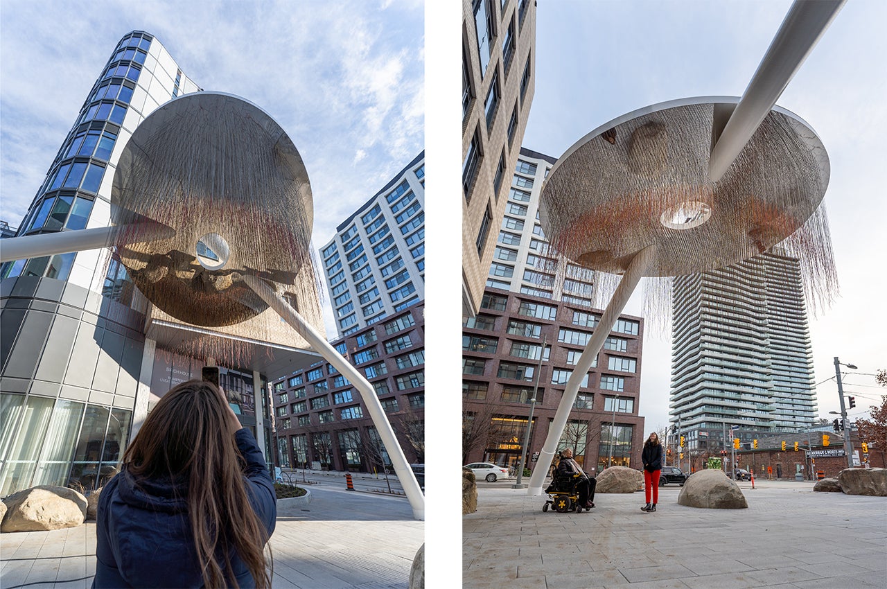 Two photographs of an individual taking pictures with the two legged art piece that stands tall over their head.