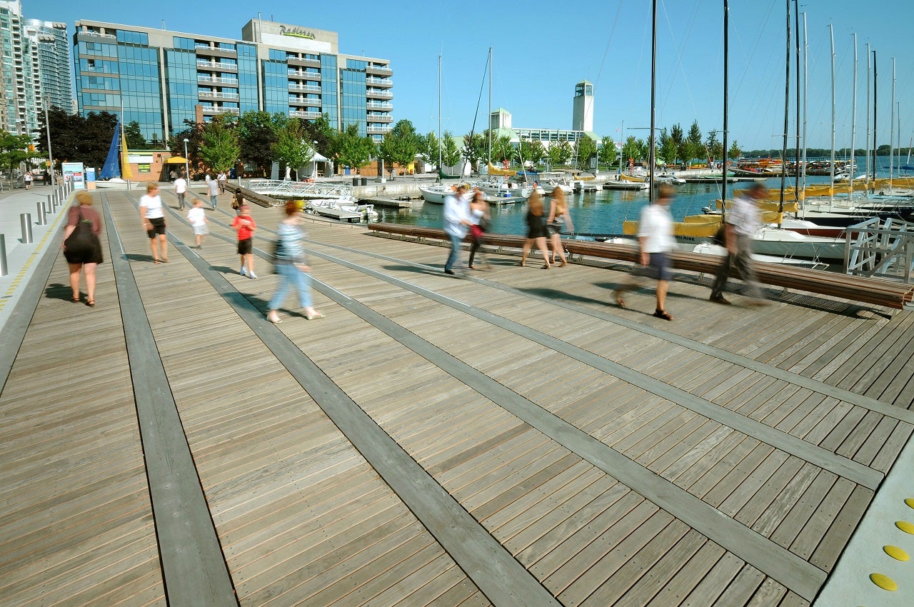 People strolling along a wooden wavedeck next to the waterfront on a sunny day.