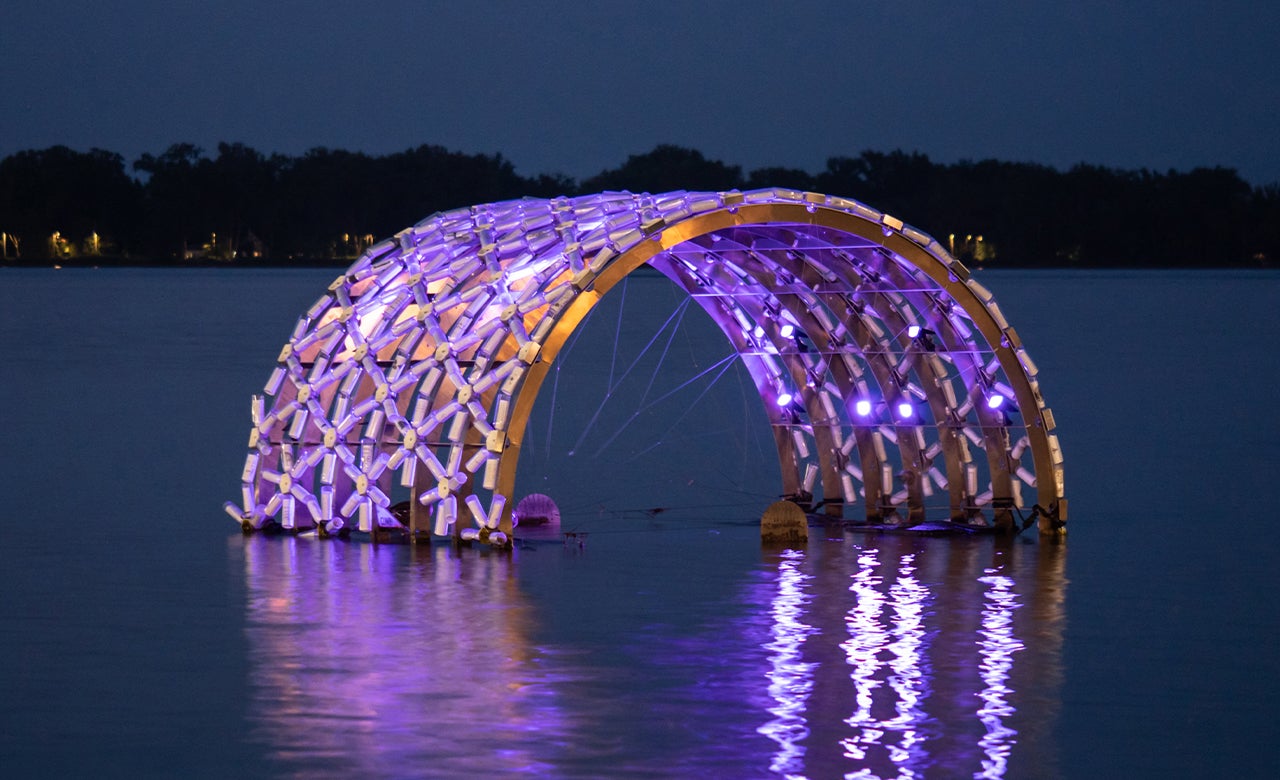 Floating public art lit up in the lake at night.