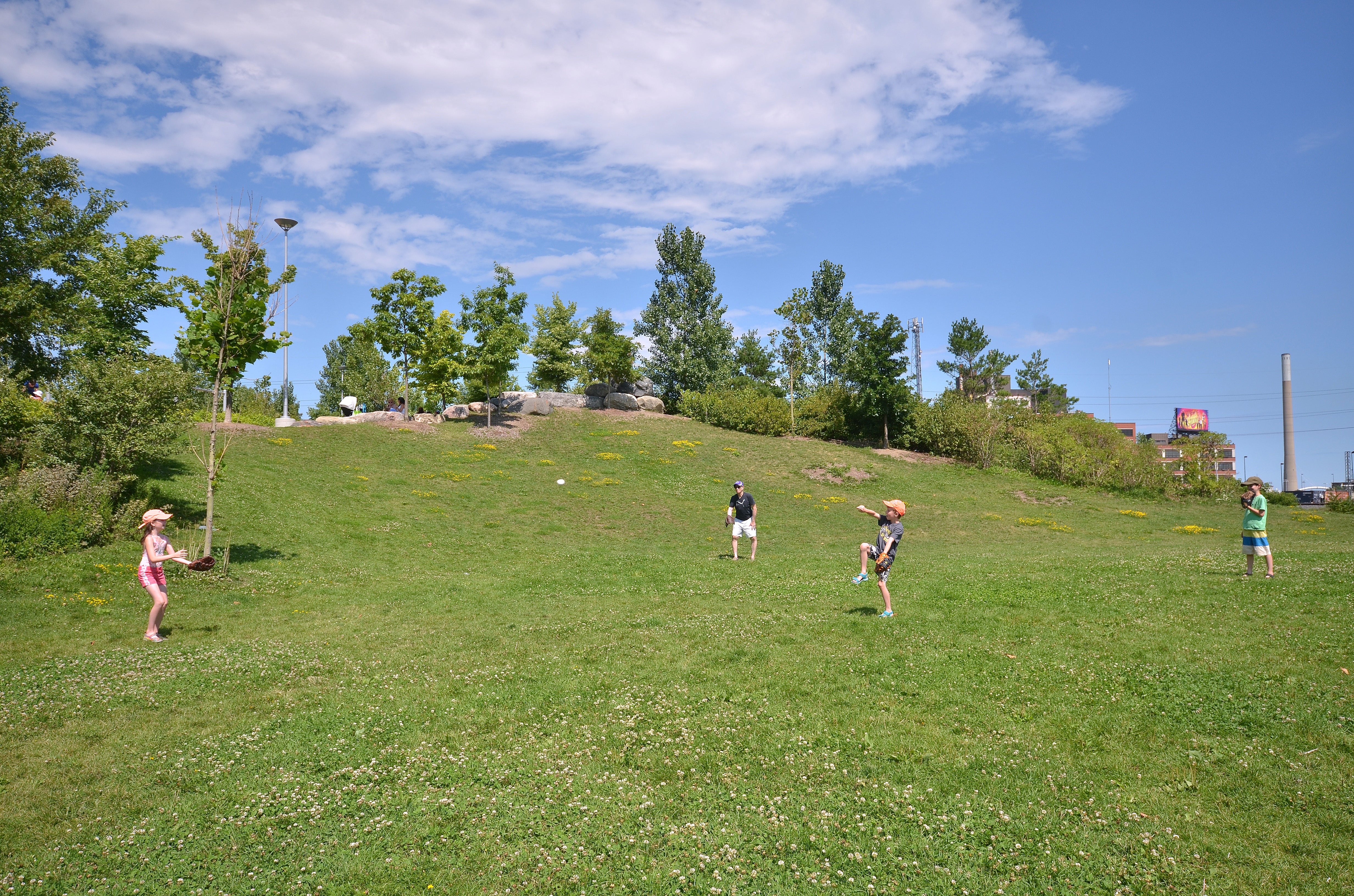 A young family plays catch on the gently sloping hills at Corktown Common.