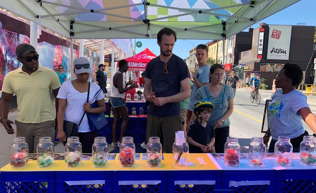 People at a street festival examining glass jars with candies in them.