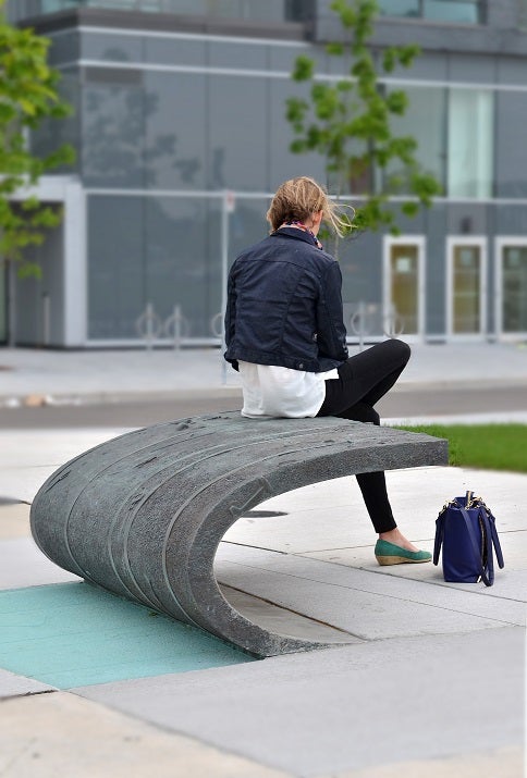 A woman sits on a piece of concrete that acts as seating and public art