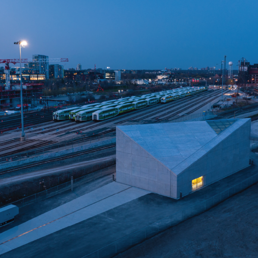 Aerial view of an angular building at dusk with a railyard in the background.