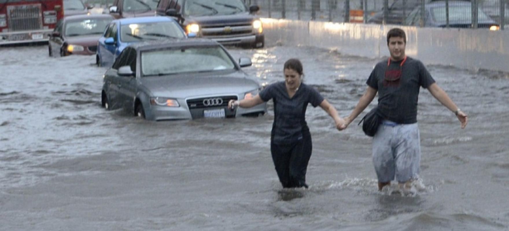cars stuck and people walking through flooded streets