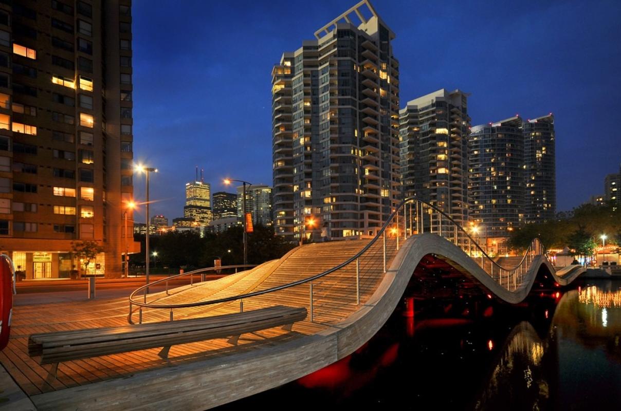 The Simcoe WaveDeck that shows the night sky, buildings lit up, and the red underlighting of the wavedeck next to Lake Ontario