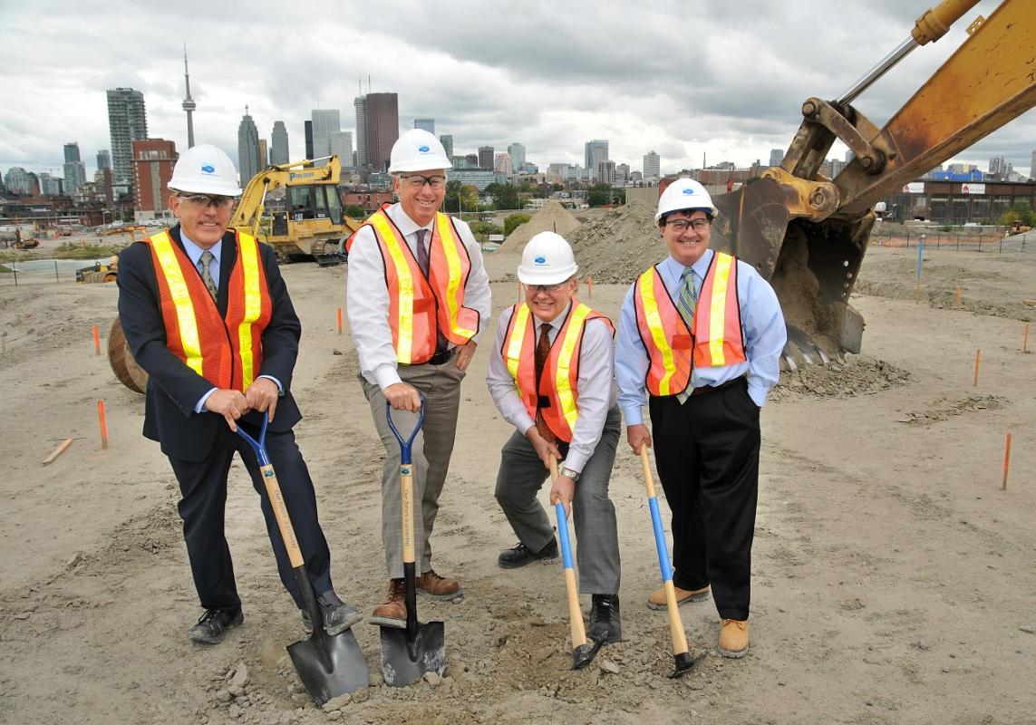 four people posing with shovels on a construction site