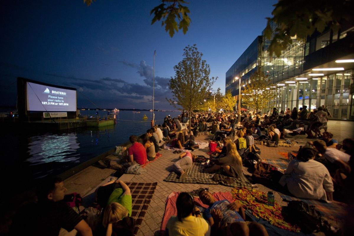 crowds gathered on the water's edge at night to watch an outdoor film