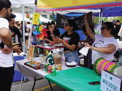 Two people at a vendor booth at a busy outdoor food market. 