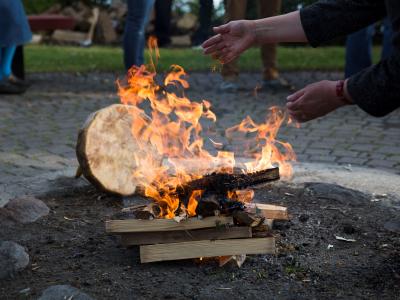 Two hands tending to a fire. A Hyde drum is behind the fire. 