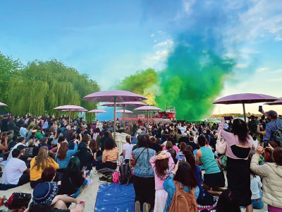 A crowd on a beach with a smoke sculpture in background.