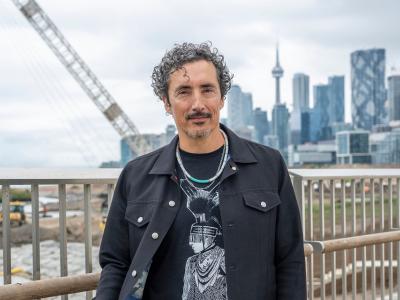 An individual dressed in black poses for the camera with Toronto's Skyline overlooking CN Tower in the backdrop.
