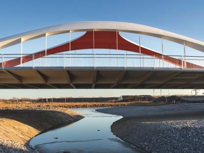 A modern bridge over a water body with concrete on the sides and sky in the background.