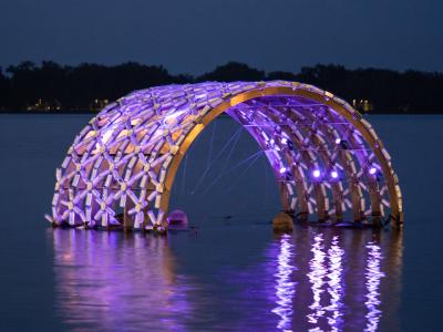 Floating public art lit up in the lake at night.