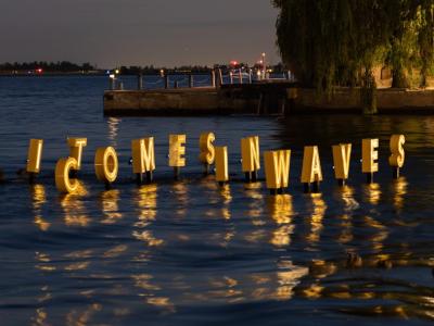 Letter IT COMES IN WAVES float and glow on water in the dark as part of a floating artwork.