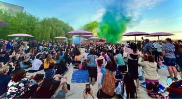 A crowd of people on a beach facing a green and blue smoke display.