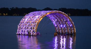 Floating public art lit up in the lake at night.