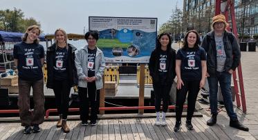 Group of six individuals wearing "U of T Trash Team" T-shirts standing in front of a board about water ecosystems.